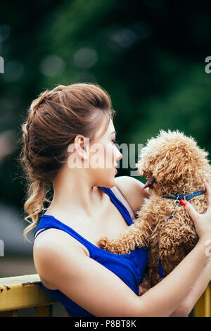 Portrait of beautiful smiling young woman with her little red poodle puppy. Stock Photo