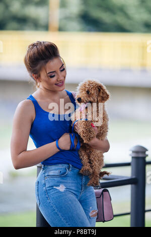 Portrait of beautiful smiling young woman with her little red poodle puppy. Stock Photo