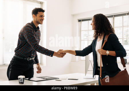 Businessman greeting a woman entrepreneur at his table by shaking hand. Businesswoman carrying office bag shaking hand with a business colleague at hi Stock Photo