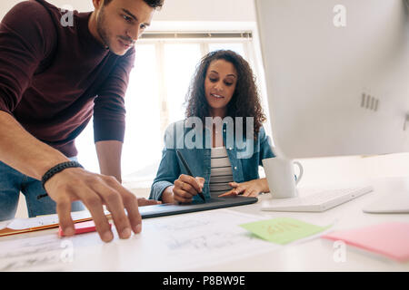 Businessman looking at business papers while the woman is writing on the digital writing pad. Business partners working together in office. Stock Photo