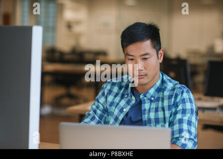 Focused young Asian designer using a laptop at his desk Stock Photo