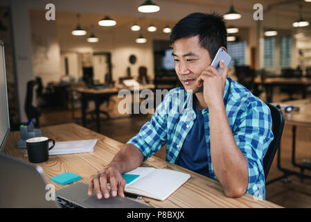 Smiling Asian designer talking on a cellphone and working online Stock Photo