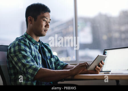 Young Asian designer using a tablet at his office workstation Stock Photo