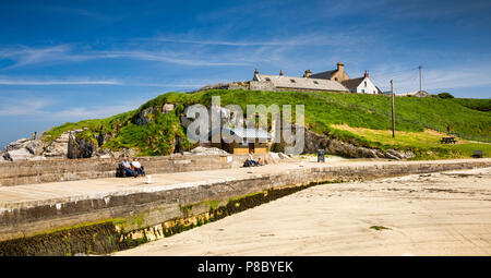 UK, Northern Ireland, Co Antrim, Islandmagee, Portmuck, visitors sitting in sun on harbour wall, panoramic Stock Photo
