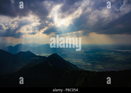 sunbeams shining bright through dark and heavy clouds over mountains and landscape a thunderstorm atmosphere mountain peak bavarian alps nearby munich Stock Photo