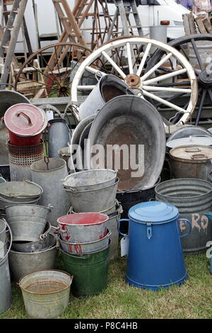 Group of old antique galvanised iron buckets and tin baths on display with various other vintage items including cart wheels Stock Photo
