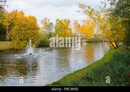 A small decorative fountain in the middle of a transparent lake against the backdrop of beautiful autumn trees . For your design Stock Photo