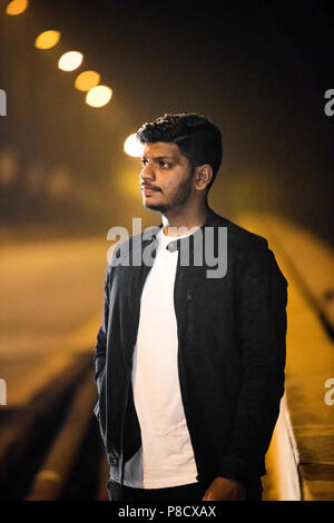 Waist up, outdoor portrait of a young adult Indian boy in black casual jacket over bokeh background. Stock Photo