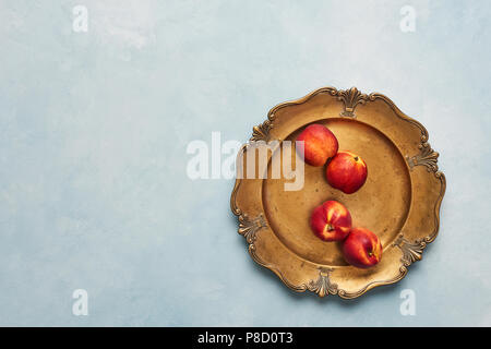 Flat lay of fresh nectarines fruits on rustic golden serving plate on light blue background. Top view with copy space. Stock Photo