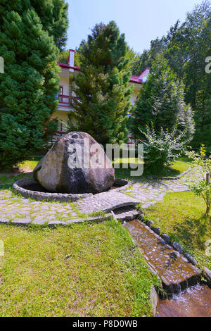 a large stone from which the fountain flows along the background of large juniper trees . For your design Stock Photo