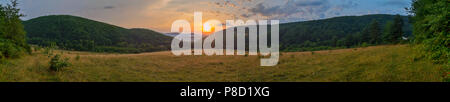 Panoramic photo of the sunset. The sun hides behind the green hills . For your design Stock Photo