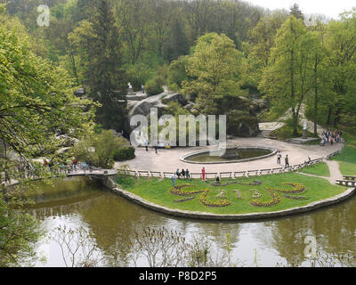 A large number of tourists stroll through the park with green decorative lawns, lakes with bridges and beautiful stone boulders . For your design Stock Photo