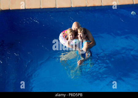 Grandparents with two year old granddaughter floating in an inflatable ring in a holiday swimming pool Stock Photo