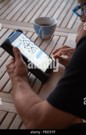 A senior man working on the New York Times crossword online on an iPad Stock Photo