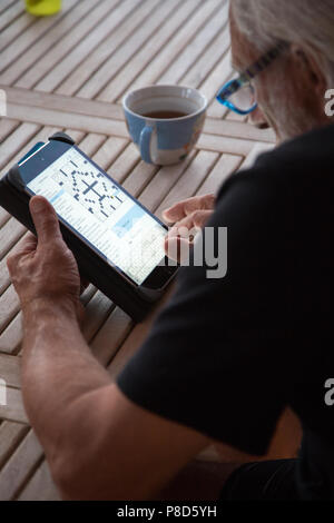 A senior man working on the New York Times crossword online on an iPad Stock Photo