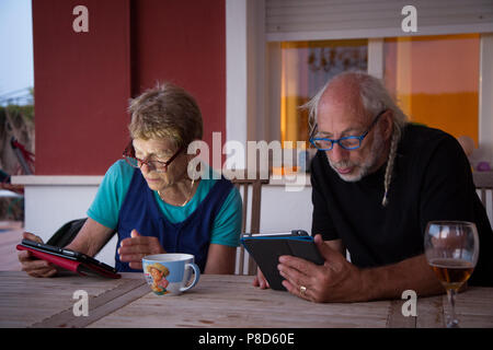 Senior citizens browse tablets sitting outside on a summer evening at a table Stock Photo