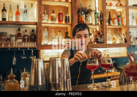 Young female bartender standing behind a bar counter making cocktails  Stock Photo