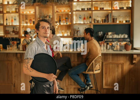 Waiter standing in a trendy bar ready to serve customers Stock Photo