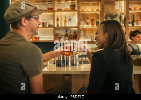 Two smiling friends sitting in a bar cheering with drinks Stock Photo