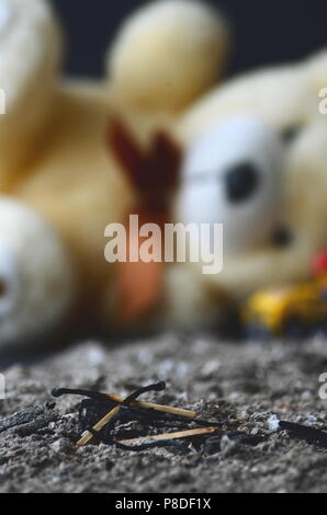 Aftermath of a house fire. Matches on cold ashes with a teddy bear in the background. Concept of children's safety, fire hazard, danger, arson. Stock Photo