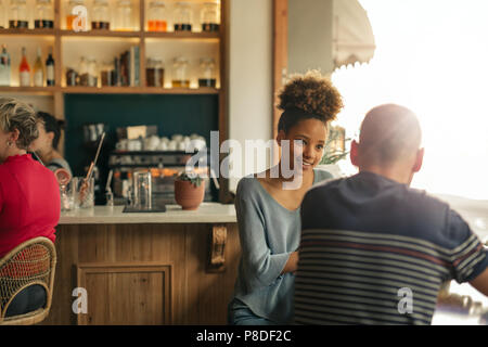 Smiling young woman talking with her friend in a bar Stock Photo
