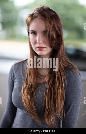 Portrait of the face of a pretty girl standing outdoors and confidently looking at the camera. Selective focus. Waist up. Stock Photo