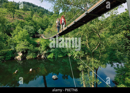 Woman and man crossing suspension bridge over river Stock Photo