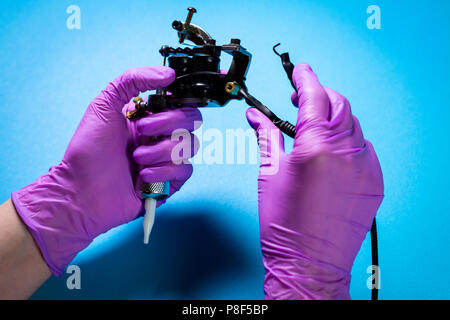 Hands In Pink Rubber Gloves Hold A Tattoo Machine On A Blue Background Stock Photo