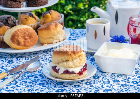 Afternoon tea with cakes and traditional English scones with strawberry jam and clotted cream set up on a table in the garden. Outdoor dining. Stock Photo