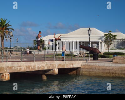 Local Bermudian kids diving from bridge railing into water near Ordnance Island, Bermuda Stock Photo
