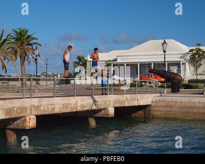 Local Bermudian kids diving from bridge railing into water near Ordnance Island, Bermuda Stock Photo