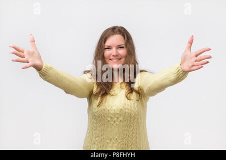 portrait of attractive smiling caucasian woman raised up arms hands at you. She is dressed in yellow sweater. Happy to welcome a friend or guest. I wa Stock Photo