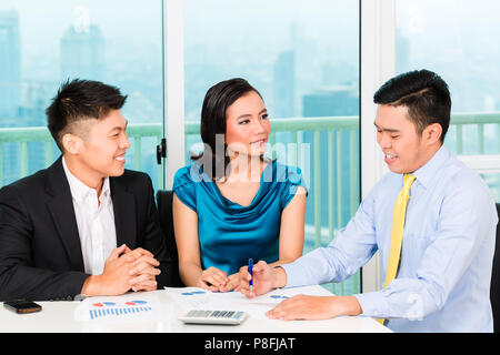 Asian banker selling insurance to couple in office Stock Photo