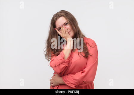 Closeup of tired plump european woman in red shirt. She is looking trhough fingers at camera. Concept of depressed person mood. She is tired and need  Stock Photo