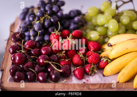 Fruits (white and blue grapes, baby bananas, strawberries and cherries) on a wooden plate Stock Photo