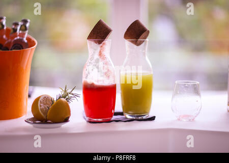 Two bottles with lemonade (mint and forest fruits), an empty dirty glass and a sliced lemon with rosemary on a bar Stock Photo