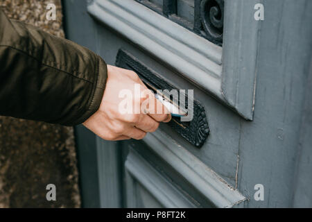 The postman puts a letter or newspaper or magazine in the mailbox at the door of a residential building or a person puts a brochure with advertising.  Stock Photo