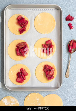 Shortcrust pastry circles on a baking tray filled with spoonfuls of roasted rhubarb. Stock Photo
