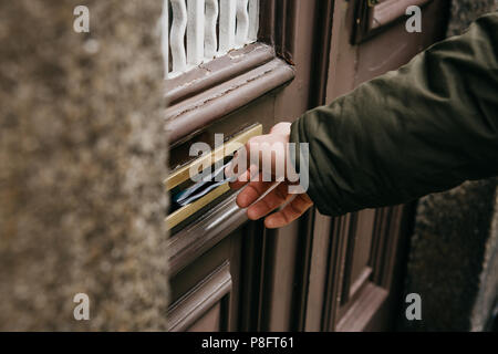 The postman puts a letter or newspaper or magazine in the mailbox at the door of a residential building or a person puts a brochure with advertising.  Stock Photo