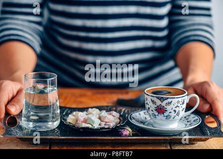 A woman serving Turkish coffee in a traditional Turkish coffee cup on a traditional copper tray. A glass of water with a rose petal inside and Turkish Stock Photo