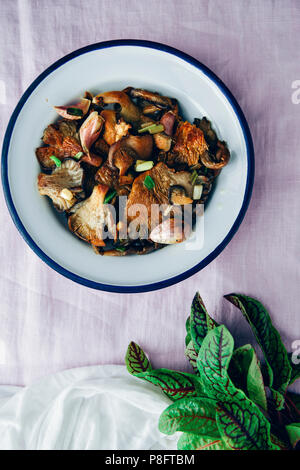 Fried oyster mushrooms served in a white bowl on a light pink background photographed from top view. Herbs accompany on the side. Stock Photo