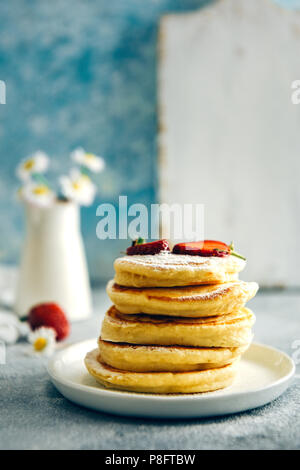 Almond milk pancakes topped with strawberries and powdered sugar stacked on a white plate photographed from front view. Strawberries and flowers accom Stock Photo