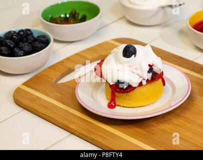 Preparing shortcake dessert with fresh strawberries, blueberries, and whipped cream. Stock Photo