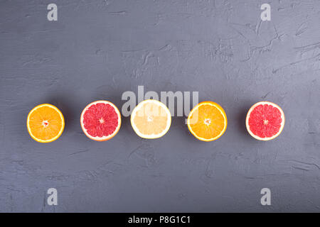 Citrus fruits with assorted slices and juice in a glass. Gray stone background. Vitamins and health in food. Copy space Stock Photo