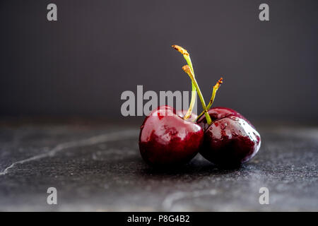 Three juicy ripe dark red cherries on slate surface against black background Stock Photo