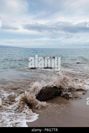 Wave breaks over a small rock at a beach on the west coast of Maui Stock Photo