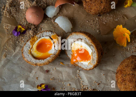 Scotch egg cut open with egg yolk oozing out on parchment paper with wild flowers Stock Photo