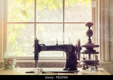 Old-fashioned sewing machine and accessories displayed next to a window. Textured and filtered to look like an old photograph, with light leaks giving Stock Photo