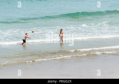 Two men play volleyball on the shore of the Atlantic ocean as its waves hit the sandy beach at the village of St Agnes, Cornwall, England. Stock Photo