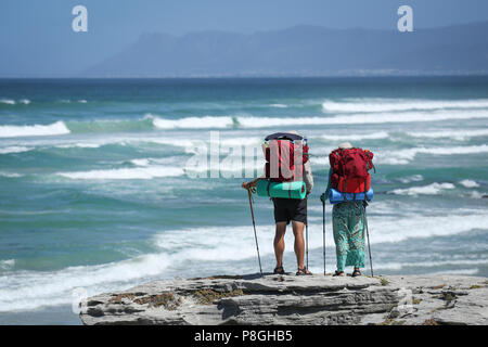 Two hikers standing on a cliff enjoying the view of the sea and mountains. Stock Photo